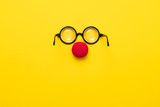 Fototapeta  - Funny glasses, red clown nose and tie lie on a colored background, like a face.