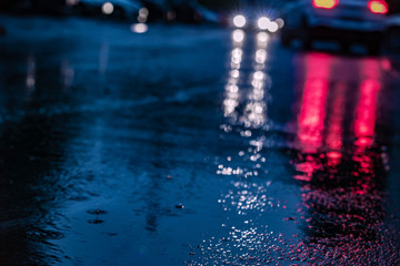 Night road blurred. Headlight of car in the dark while heavy raining. Rain in the city. Road, pavement, close up. Water splashes, spills on roadway