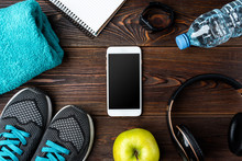 Fitness Bracelet, Sneakers, Mobile Phone And Bottle Of Water On Dark Wooden Background.
