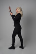 © faestock - full length portrait of a blonde girl wearing  modern black jacket and pants, standing pose  facing away from the camera on grey studio background.