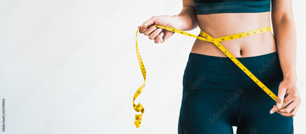 Close up shot of woman with slim body measuring her waistline and torso. Healthy nutrition and weight losing concept. - obrazy, fototapety, plakaty 