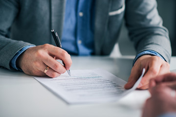 Wall Mural - Businessman sitting at desk holding and pen signing contract paper, employment or partnership agreement.