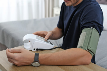 Wall Mural - Man checking blood pressure with sphygmomanometer at table indoors, closeup. Cardiology concept