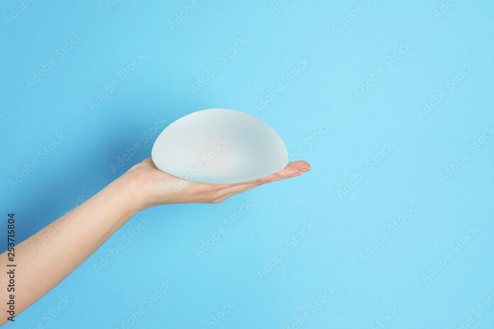 Woman holding silicone implant for breast augmentation on color background, space for text. Cosmetic surgery - obrazy, fototapety, plakaty 