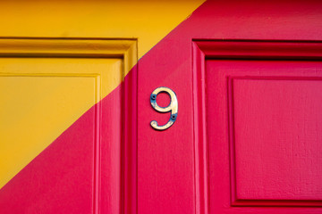 House number nine on a brightly painted red and yellow wooden house door with a diagonal stripe and the 9 in bronze