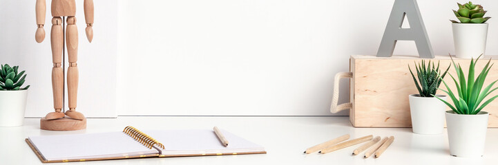 White desk next to an empty wall with space for text. Copy space. Green succulents as decoration. Open notebook and wooden figure of a man. Office supplies. Panorama