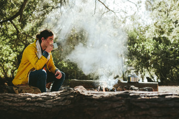 Wall Mural - Man camping in forest sitting near a bonfire