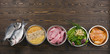 Panorama banner with healthy pet food ingredients with chopped raw turkey, fish, groats, greens and grains in individual bowls on brown wooden background. Flat lay.