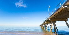 Clear Calm Blue Sky Day With A Long Wooden Pier Vanishing To The Horizon. Glenelg Beach, South Australia. Copy Space.