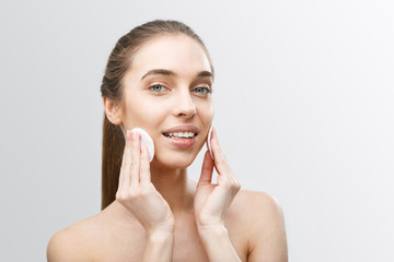 Close up beauty portrait of a happy young woman with soft healthy skin removing make up with cotton pad and looking at camera