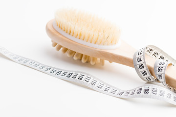 Dry massage brush with tape measure on white desk. Health and diet.