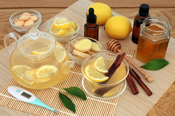 Medicinal cold and flu remedy with thermometer, eucalyptus and tea tree oil, ginger, cinnamon sticks, vitamin c tablets, lemon fruit and honey with hot drink on bamboo and oak.