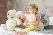 Portrait of child girl having fun sitting and playing with a teddy bears on a bed