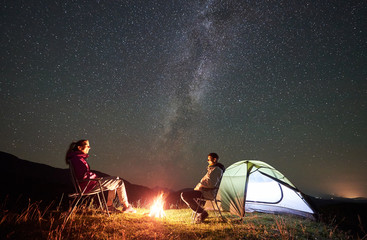 happy couple tourists resting at summer night camping in the mountains. smiling man and woman sittin