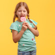 © Max - Cute little girl licks candy and laughs in the studio on a yellow background