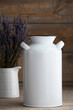 © Sarah - Mockup of a white vintage milk jug next to a vase of lavender on a brown wooden table.