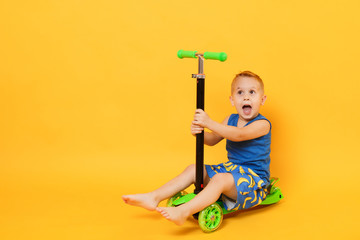 kid boy 3-4 years old wearing blue beach summer clothes on scooter isolated on bright yellow orange 