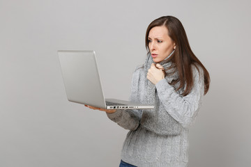 Wall Mural - Dissatisfied young woman in gray sweater, scarf working on laptop pc computer isolated on grey wall background. Healthy lifestyle online treatment consulting, cold season concept. Mock up copy space.