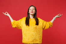 Relaxed Young Woman In Yellow Fur Sweater With Closed Eyes Hold Hands In Yoga Gesture, Meditating Isolated On Red Background In Studio. People Sincere Emotions, Lifestyle Concept. Mock Up Copy Space.