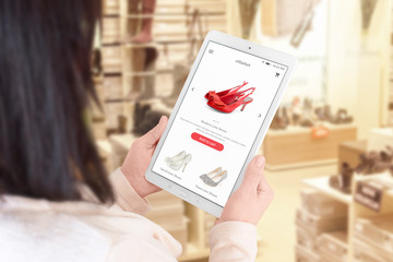 Wall Mural - Online shopping app on tablet display. Woman use tablet to search ecommerce web site. Shoe store in background.