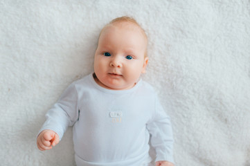 Adorable lovely newborn male baby with blue eyes lifestyle indoor portrait from above. Cute child with hands apart lying on back in pijama on bed at home. Little child with emotional face rest on sofa