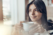 © Ivan - Beautiful caucasian girl in casual clothes with coffe in hands smiling while sitting in cafe. success. Close up, with light leaks