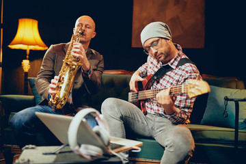 Wall Mural - Two talented musicians playing bass gutar and sax while sitting on couch in home studio.