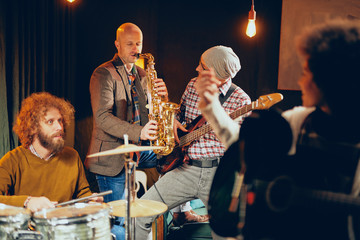 Sticker - Multicultural band practicing for the gig in home studio. In foreground mixed race singer and in background drummer and saxophonist.