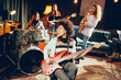 © chika_milan - Girls playing jazz music. In foreground one woman playing bass guitar and in background other three playing acoustic guitar, saxophone and drums. Home studio interior.