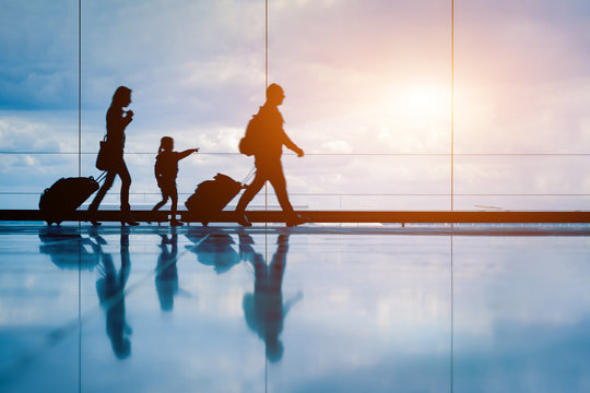 family at airport travelling with young child and luggage walking to departure gate, girl pointing a
