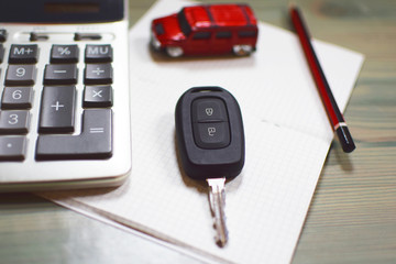 Calculator, toy car, red pencil, car keys and notebook on wooden texture background, shallow depth of field. Planning to rent, buy or insurance car concept.