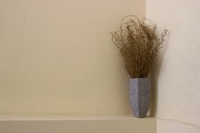 Golden Colored Ornamental Bouquet Of Dried Plant In A Grey Floral Ceramic Large Vase Isolated At The Niche Of A Beige Painted Wall