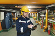 © dusanpetkovic1 - Caucasian worker in protective suit, helmet and antifones on ears using tablet for work while standing in heavy industry plant.