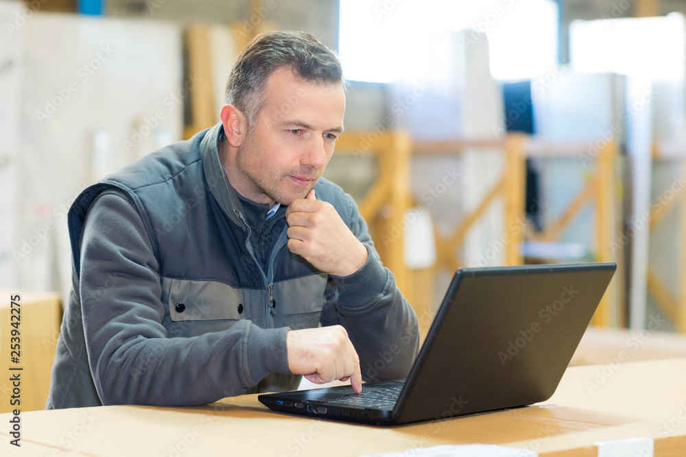 male worker looking at laptop in workshop - obrazy, fototapety, plakaty 
