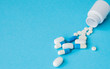 Close up pills spilling out of pill bottle on blue background. Medicine, medical insurance or pharmacy concept
