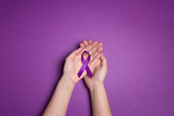 Wall Mural - Hands holding Purple ribbons on a purple background. World epilepsy day.