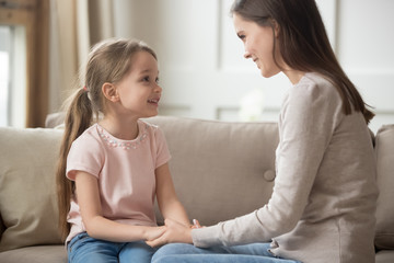 loving mother and child holding hands talking sitting on sofa