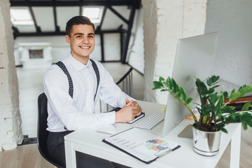 Wall Mural - Young  attractive smiling businessman with laptop and notebook paper sitting at his work place .