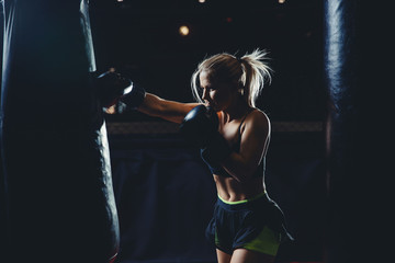 Concept female sport. Strong athletic young blond woman is training self-defense punches in boxing gloves