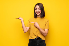 Young Woman Over Yellow Wall Holding Copyspace Imaginary On The Palm To Insert An Ad