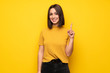 © luismolinero - Young woman over yellow wall showing and lifting a finger in sign of the best
