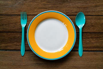 Empty color plate, fork and spoon on wooden table background, top view with copy space