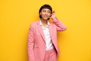 Wall Mural - Modern woman with pink business suit listening to something by putting hand on the ear