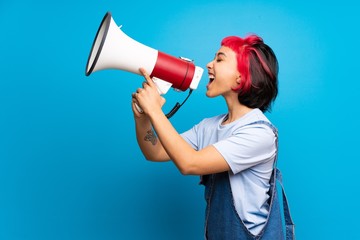 Wall Mural - Young woman with pink hair over blue wall shouting through a megaphone
