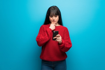 Woman with red sweater over blue wall thinking and sending a message