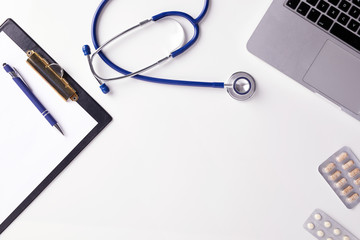 Wall Mural - Top view of doctor desk with stethoscope, latptop, pills and blank paper on clipboard with copy space, flat lay shot.