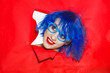 Portrait of an extravagant woman with blue hair and glasses looking through hole in paper wall