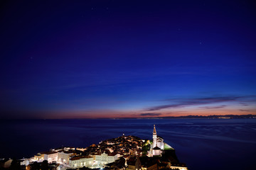 Stars over Piran Slovenia at night with lit Tartini Square Courthouse City Hall and St George's Cathedral with lights of Itlay in distance