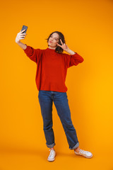 Sticker - Excited emotional young pretty woman posing isolated over yellow wall background take selfie by mobile phone.