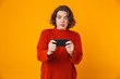 © Drobot Dean - Emotional young pretty woman posing isolated over yellow wall background play games by mobile phone.